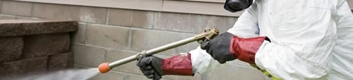 Pest control technician applying exterior insect treatment along a home foundation in Anchorage, AK