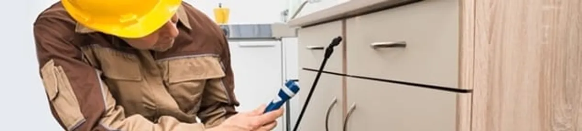 Roach exterminator applying treatment under kitchen cabinets in Anchorage, AK