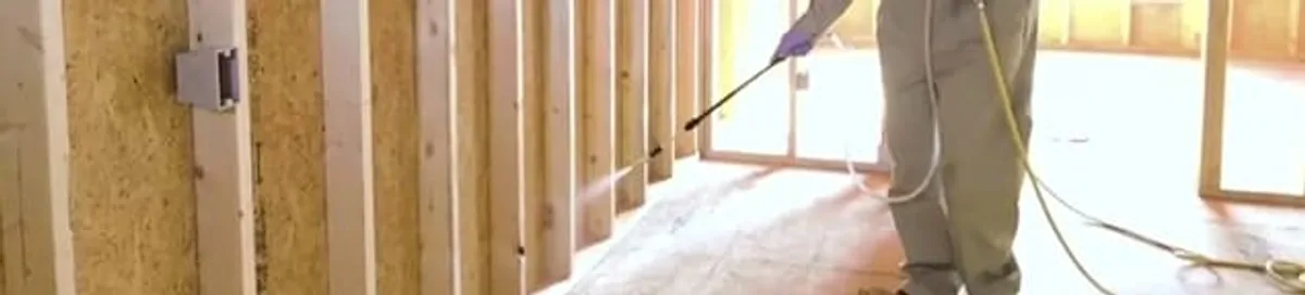 Termite treatment technician applying spray along framing and unfinished walls in Anchorage, AK